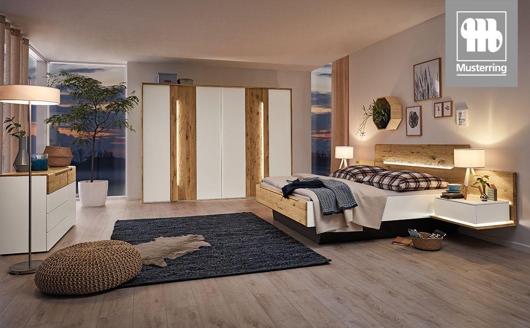 Schlafzimmer mit beleuchtetem Bett und Kleiderschrank in Holz-Weiß-Kombination.