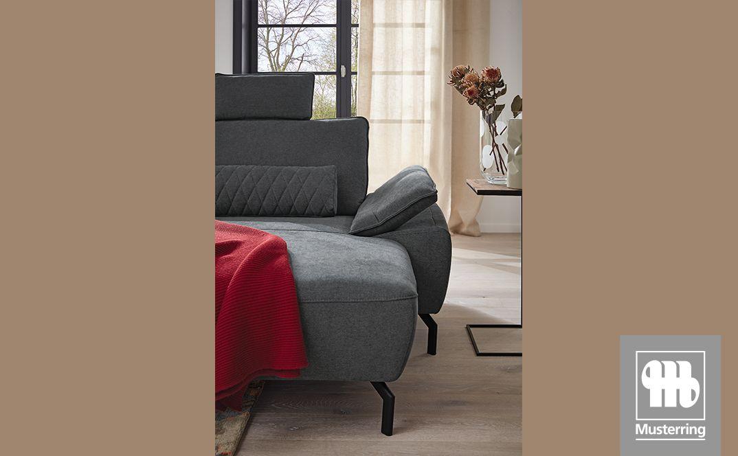 Detailansicht eines grauen Sofaelements mit Kissen und roter Decke in einem Wohnraum.