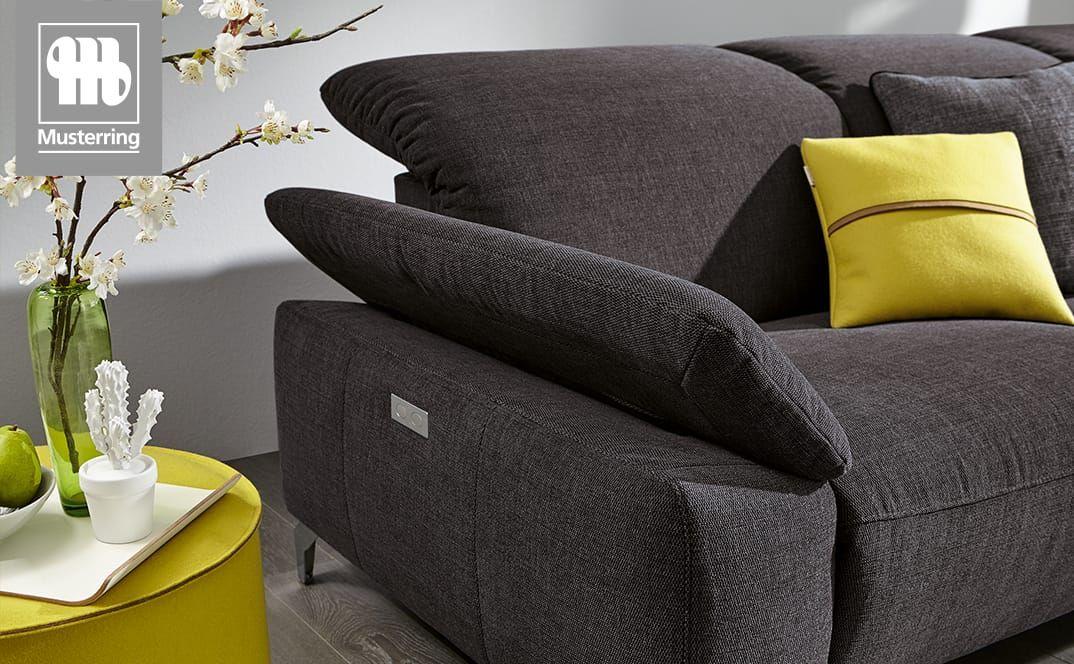 Nahaufnahme der gepolsterten Armlehne eines Sofas mit gelbem Kissen und Beistelltisch.