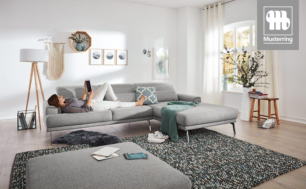 Graues Ecksofa in hellem Wohnzimmer, Frau liegt entspannt darauf.