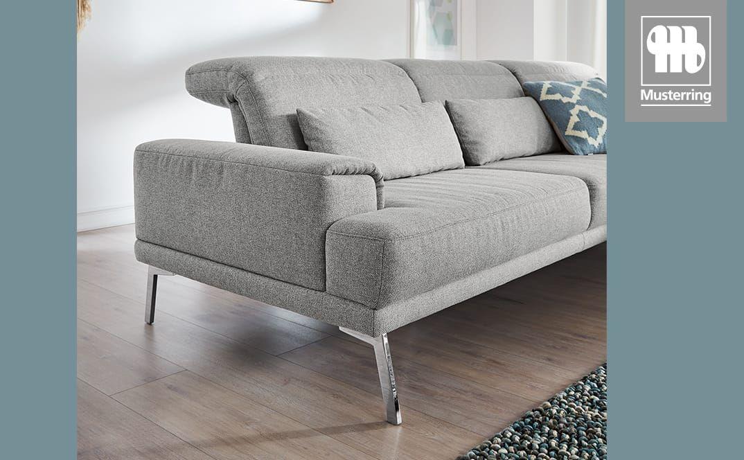 Detailansicht eines grauen Sofas mit gepolsterter Armlehne und Metallfüßen.