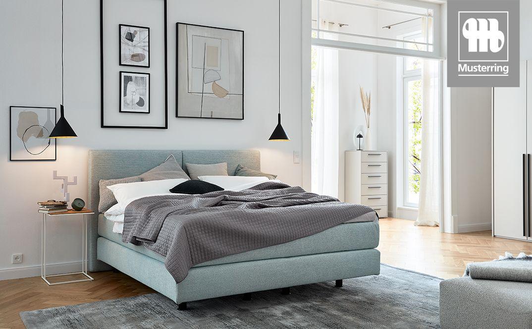 Boxspringbett Elias von Musterring in hellblauer Stoffausführung in modernem, lichtdurchflutetem Schlafzimmer.