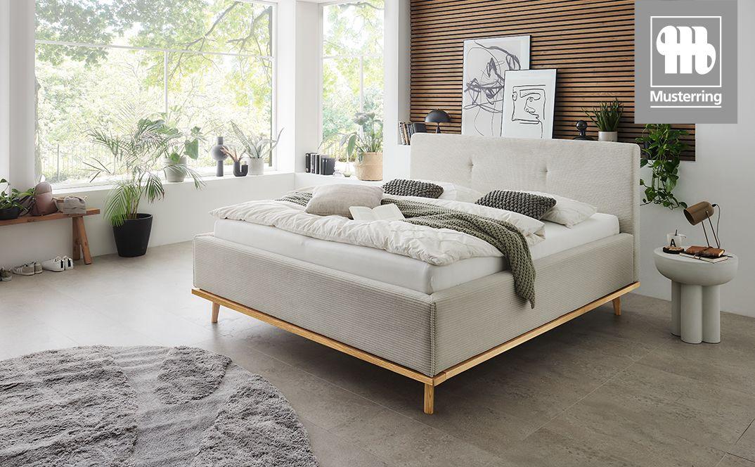Polsterbett Delphi von Musterring in hellem Stoff mit Holzgestell in modern eingerichtetem Schlafzimmer.