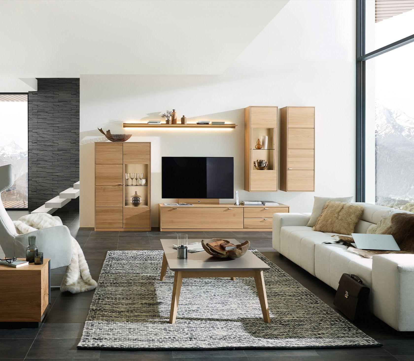 Wohnwand „Concetto" in Holz-Naturdekor mit TV-Lowboard, Highboard und Wandvitrine, kombiniert mit cremefarbenen Sofas und Couchtisch.