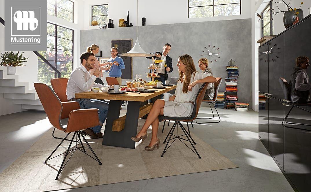 Gruppe von Menschen beim gemeinsamen Essen an einem großen Esstisch mit modernen Stühlen.