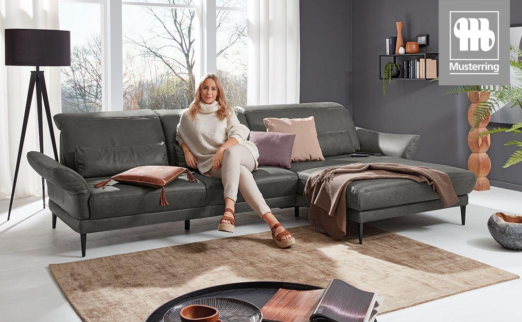 Großes graues Ecksofa in heller Wohnumgebung mit sitzender Frau und Dekokissen.