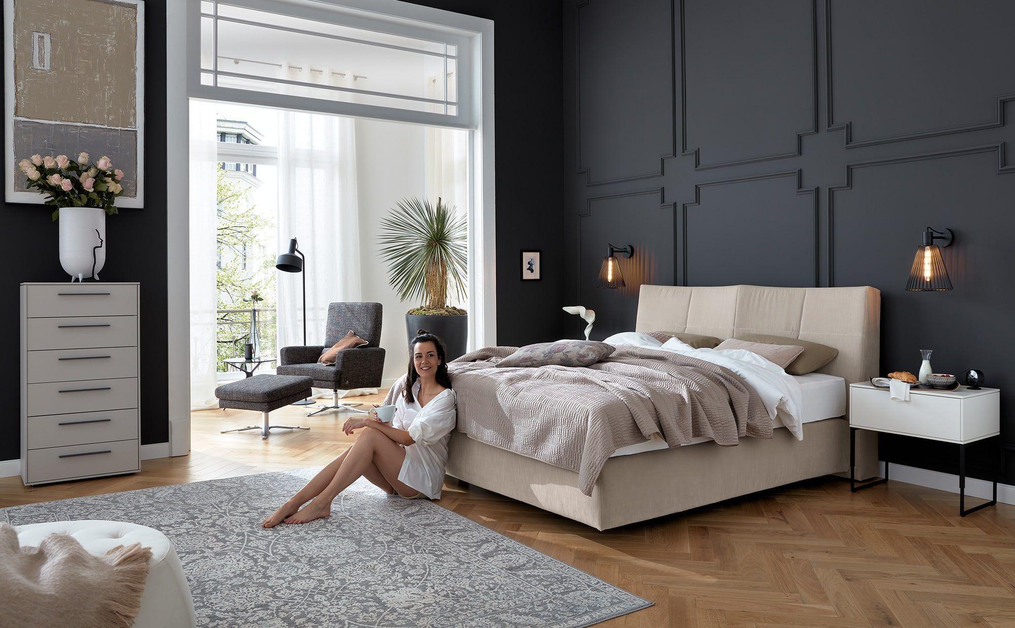 Boxspringbett Elias von Musterring in beiger Stoffausführung in elegantem Schlafzimmer mit dunkler Akzentwand.